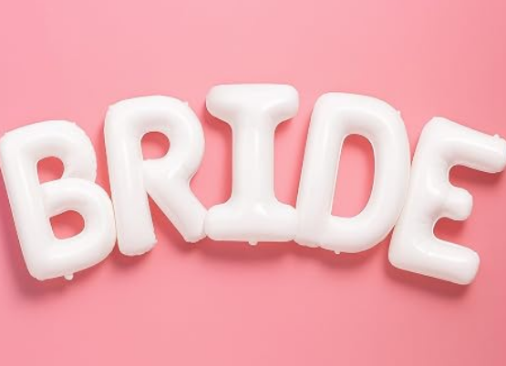 Giant white BRIDE letter balloons above a bed in a bachelorette Airbnb